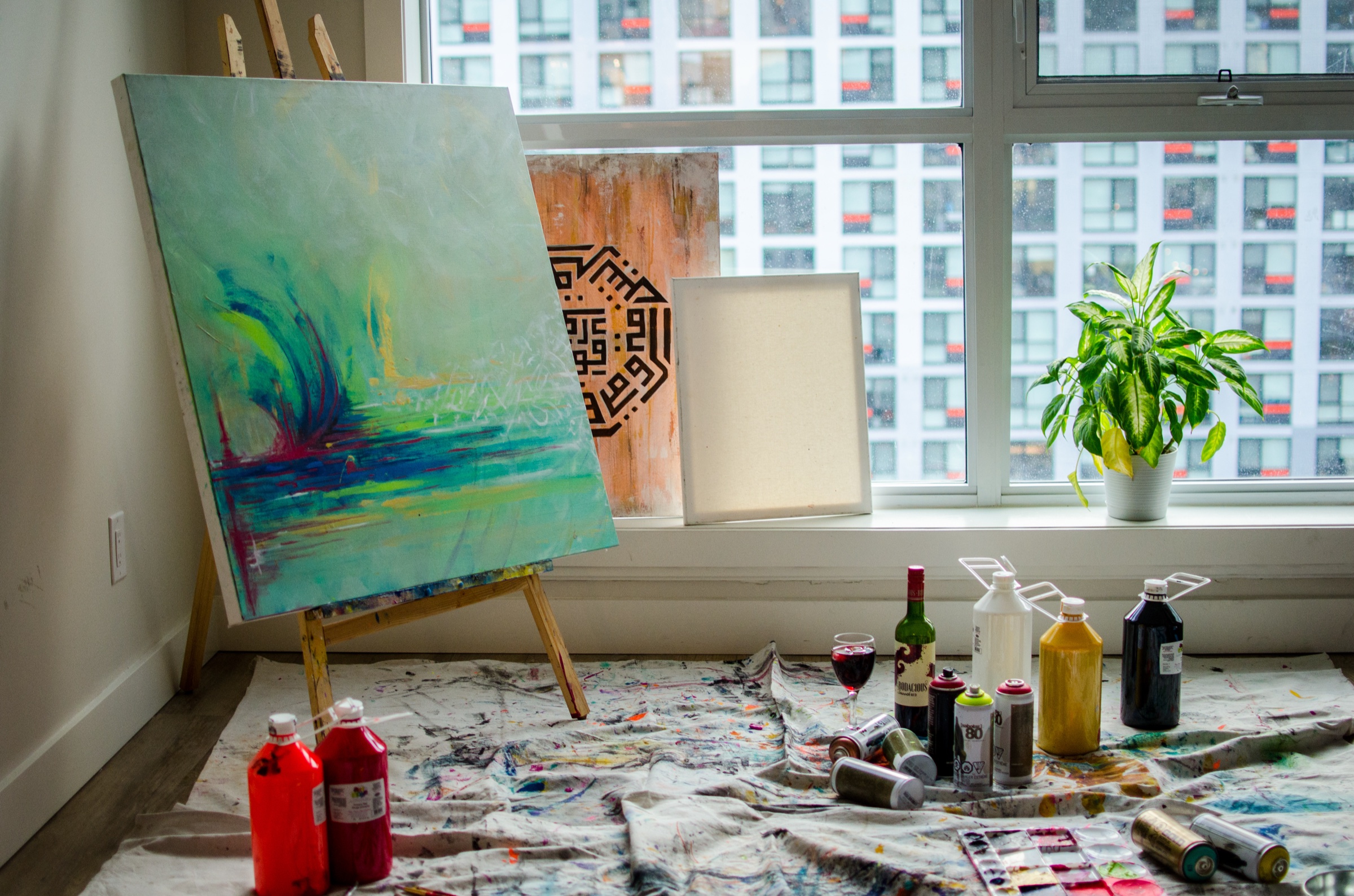 Faith's studio: an easel by a tall window, paints laid out on the floor